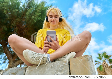 Teenage girl in headphones looking in smartphone Teenage girl in headphones looking in smartphone 85706896