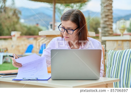 Middle aged woman working remotely using a laptop. Middle aged woman working remotely using a laptop. 85706897