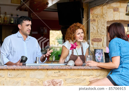 Couple working at the bar in an outdoor cafe talking to a female client 85706915