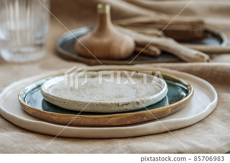 Table setting with Handmade craft plates on linen tablecloth and wood accessories in earth tones 85706983