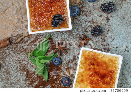 Creme brulee with cracked sugar crust, wild berries and spices on turquoise clay backdrop Creme brulee with cracked sugar crust, wild berries and spices on turquoise clay backdrop 85706999