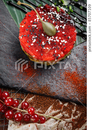 Tuna tartar with avocado and caviar, decorated with spices, lime and cucumber, red currants plated on banana leaf. Macro close up tuna tartar 85707109