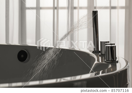 Spout running water from wide bath tube faucet into a hot Jacuzzi Spout running water from wide bath tube faucet into a hot Jacuzzi 85707116