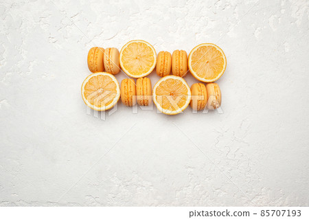 Orange French Macaroons with orange fruit filling on a creamy white clay background, decorated with fresh sliced oranges 85707193