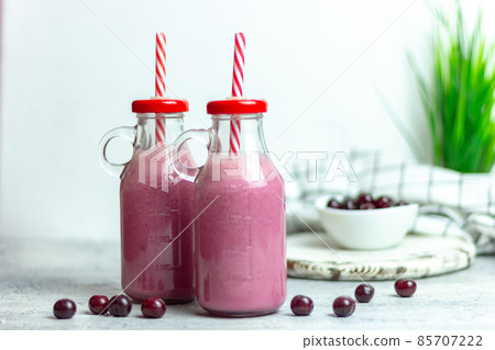 A bottle of cherry smoothies on a white background, cherries in bulk and in a plate. Morning summer breakfast 85707222