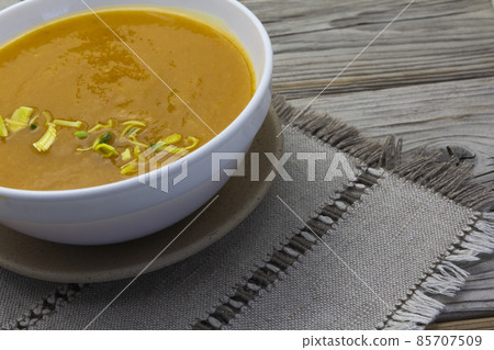 Thick and Creamy Pumpkin Soup in white bowl on wooden rustic background, linen napkin. Healthy eating, horizontal. 85707509