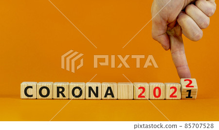 Symbol of covid-19 pandemic in 2022. Doctor turns wooden cubes and changes words 'corona 2021' to 'corona 2022'. Beautiful orange background, copy space. Medical, covid-19 pandemic in 2022 concept. 85707528