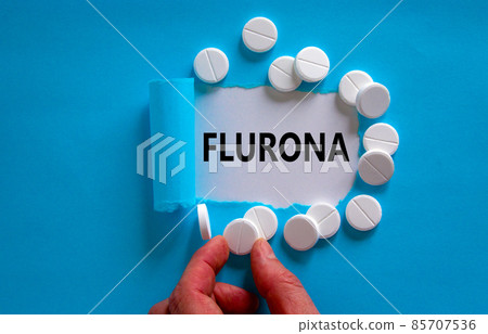 Covid-19 corona and flu flurona symbol. The word flurona appearing behind torn blue paper. White pills. Doctor hand. Blue background. Medical, covid-19 corona and flu flurona concept. Copy space. 85707536