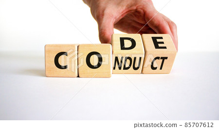 Code of conduct symbol. Businessman turns the wooden cube and changes the word code to conduct. Beautiful white background. Business and code of conduct concept. Copy space. Code of conduct symbol. Businessman turns the wooden cube and changes the word code to conduct. Beautiful white background. Business and code of conduct concept. Copy space. 85707612