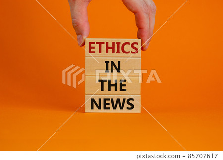 Ethics in the news concept. Wooden blocks with words 'ethics in the news'. Male hand. Beautiful orange background. Copy space. Ethics in the news concept. Wooden blocks with words 'ethics in the news'. Male hand. Beautiful orange background. Copy space. 85707617