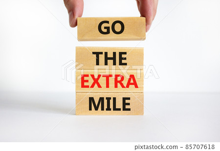 Go the extra mile symbol. Concept words Go the extra mile on wooden blocks. Businessman hand. Beautiful white table, white background, copy space. Business and go the extra mile concept. 85707618