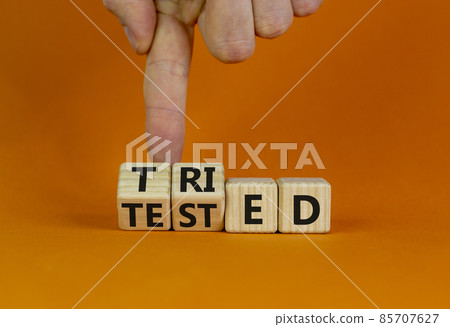 Tried and tested symbol. Businessman turns wooden cubes and changes the concept word 'tried' to 'tested' on a beautiful orange background. Copy space. Business and tried and tested concept. Tried and tested symbol. Businessman turns wooden cubes and changes the concept word 'tried' to 'tested' on a beautiful orange background. Copy space. Business and tried and tested concept. 85707627
