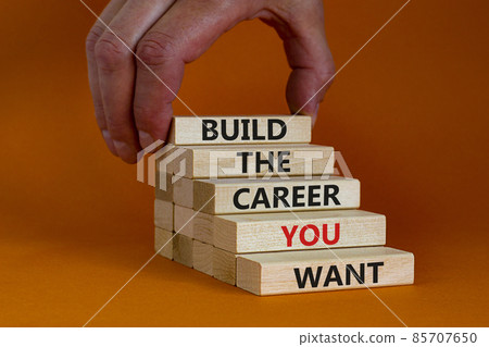 Build good career symbol. Wooden blocks with words 'build the career you want'. Businessman hand. Beautiful orange background, copy space. Business, build the career you want concept. 85707650