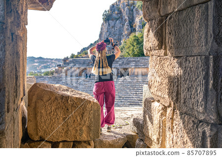 female tourist filming the ruins of antique amphitheater and famous rocky necropolis in Myra (Demre, Turkey) female tourist filming the ruins of antique amphitheater and famous rocky necropolis in Myra (Demre, Turkey) 85707895