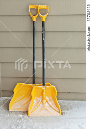 Two snow shovels dusted in snow leaning against a wall 85708426