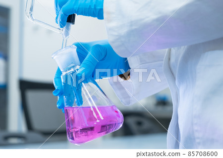 Close up scientist uses a titration method of analysis to study the chemical properties of the water sample. Scientist holding Erlenmeyer flask with pink solution Close up scientist uses a titration method of analysis to study the chemical properties of the water sample. Scientist holding Erlenmeyer flask with pink solution 85708600