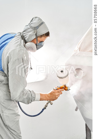 Painting the rear door of the car. Car painter in special painting chamber, wearing costume and protective gear. Car service station. Restoring a car after an accident Painting the rear door of the car. Car painter in special painting chamber, wearing costume and protective gear. Car service station. Restoring a car after an accident 85708668