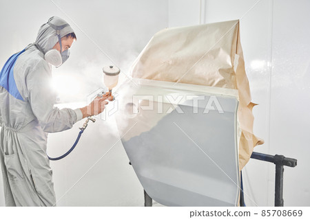 Painting the rear door of the car. Car painter in special painting chamber, wearing costume and protective gear. Car service station. Restoring a car after an accident 85708669