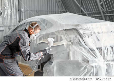 Painting the rear part of the car. Car painter wearing costume and protective gear. Car service station. Restoring a car after an accident Painting the rear part of the car. Car painter wearing costume and protective gear. Car service station. Restoring a car after an accident 85708676