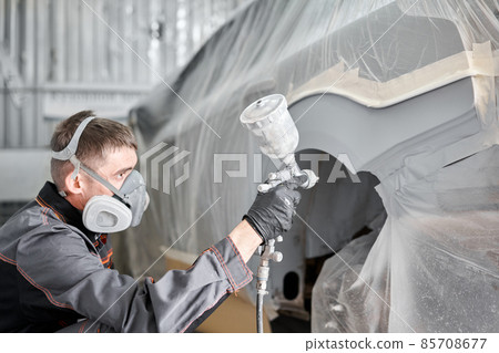 Painting the rear part of the car. Car painter wearing costume and protective gear. Car service station. Restoring a car after an accident Painting the rear part of the car. Car painter wearing costume and protective gear. Car service station. Restoring a car after an accident 85708677