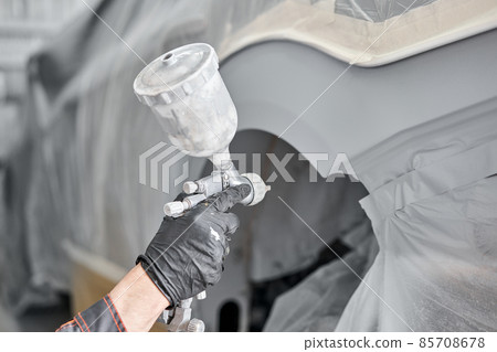 Spray gun. Worker painting parts of the car in special painting chamber, wearing costume and protective gear. Car service station. Spray gun. Worker painting parts of the car in special painting chamber, wearing costume and protective gear. Car service station. 85708678