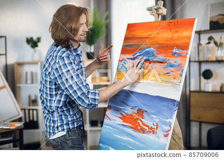 Inspired man drawing with hands on easel Inspired man drawing with hands on easel 85709006