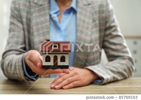 Real estate agent holding house model at wooden table, closeup Real estate agent holding house model at wooden table, closeup 85709103