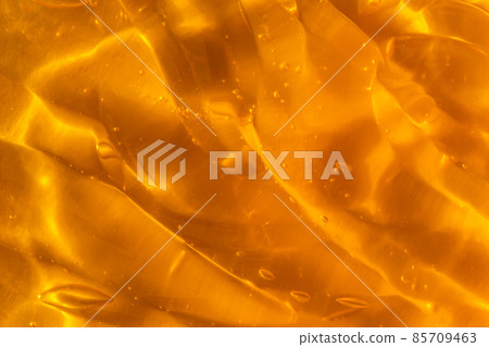 Texture of transparent yellow gel with air bubbles and waves on orange background. Concept of skin moisturizing, body care and prevention of covid19. Liquid beauty product closeup. Backdrop, flat lay 85709463