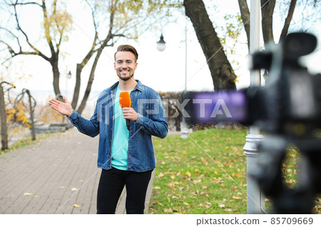 Young male journalist with microphone working in park Young male journalist with microphone working in park 85709669
