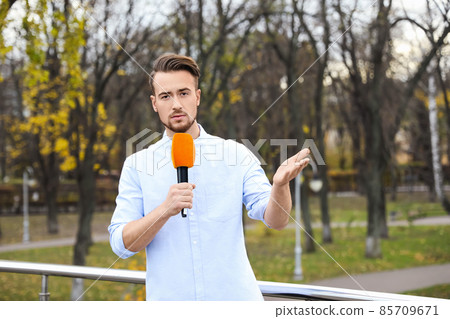 Young male journalist with microphone working in park 85709671