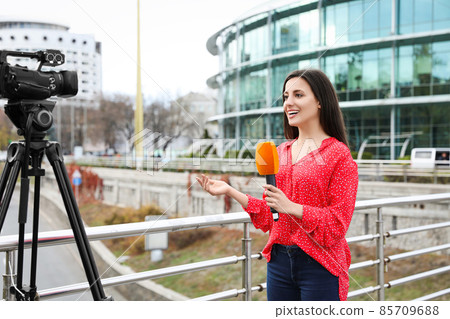 Young female journalist with microphone working on city street 85709688