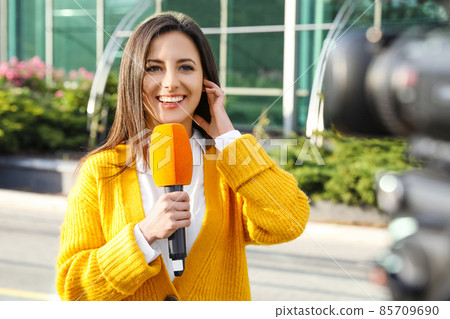 Young female journalist with microphone working on city street 85709690