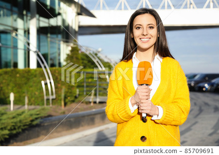 Young female journalist with microphone working on city street 85709691