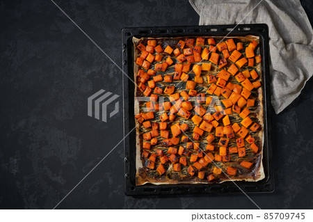 Baked pumpkin cut in small pieces on a dark baking sheet, top view. 85709745
