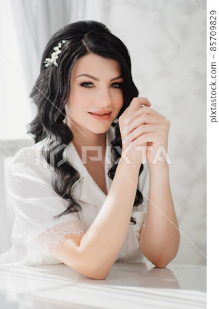 brunette bride in white silk pajamas with styling and makeup at the table 85709829