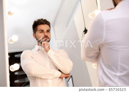 Young man looking at himself in large mirror at home 85710323