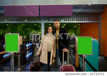 Happy young couple, man and woman, business partners standing with luggage and suitcases at the check-in counter, passing customs and passport control at the departure airport terminal. Copy space Happy young couple, man and woman, business partners standing with luggage and suitcases at the check-in counter, passing customs and passport control at the departure airport terminal. Copy space 85710751