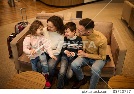 Happy family. Parents admiring their kids playing with toy planes, discussing the upcoming air trip, resting in the VIP lounge of the airport departure terminal while waiting to board the flight Happy family. Parents admiring their kids playing with toy planes, discussing the upcoming air trip, resting in the VIP lounge of the airport departure terminal while waiting to board the flight 85710757