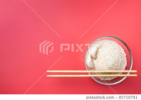 Glass bowl with rice, garlic and chopsticks on a pink background. Flat lay. Glass bowl with rice, garlic and chopsticks on a pink background. Flat lay. 85710781