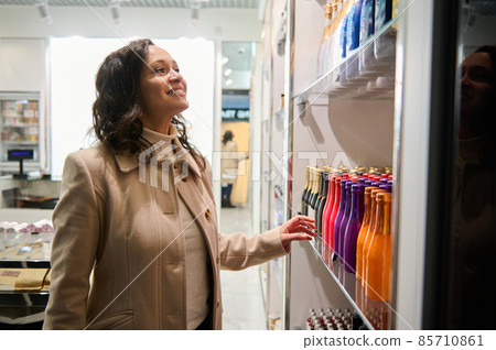 Beautiful dark-haired woman wearing beige pullover and woolen coat making purchases, shopping in duty free store while waiting for her flight in departure terminal of the International Airport Beautiful dark-haired woman wearing beige pullover and woolen coat making purchases, shopping in duty free store while waiting for her flight in departure terminal of the International Airport 85710861