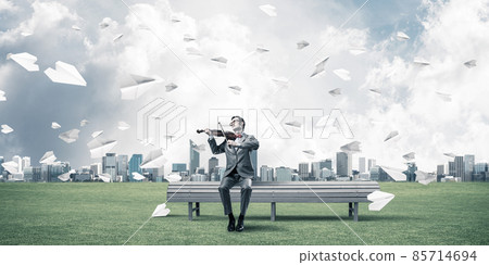 Handsome violinist in park on wooden bench play his melody Handsome violinist in park on wooden bench play his melody 85714694