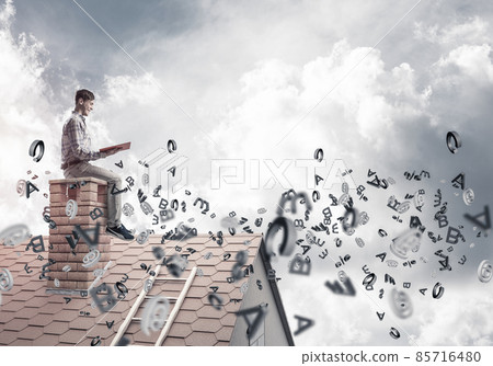 Man on brick roof reading book and symbols flying around 85716480