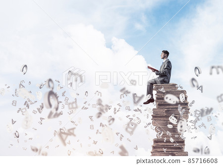 Man student on stack reading book and symbols flying around Man student on stack reading book and symbols flying around 85716608