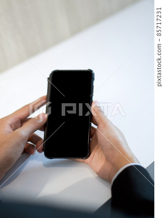 Businessman in black suit holding blank screen mobile phone with both hand. Businessman in black suit holding blank screen mobile phone with both hand. 85717231