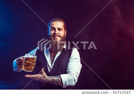 Happy bearded man holds tasty draft beer in hand while gesturing. Drinking, October fest concept. Happy bearded man holds tasty draft beer in hand while gesturing. Drinking, October fest concept. 85723587