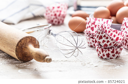 Baking utensils with eggs flour and cupcake cases on kitchen table - Close up 85724021
