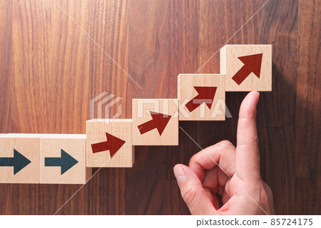 變化和成長的形象。用手指用箭頭向上推積木。一張木桌的鳥瞰圖。 變化和成長的形象。用手指用箭頭向上推積木。一張木桌的鳥瞰圖。 85724175