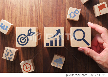 Image of business management and strategy. Hands arranging blocks with icons printed on them. A bird's-eye view of a wooden table. 85724193