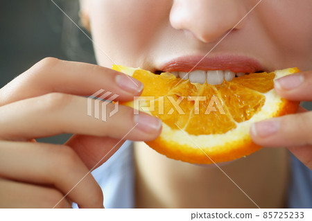 Woman hold in hand slice of chopped orange eats for breakfast with mouth in kitchen 85725233