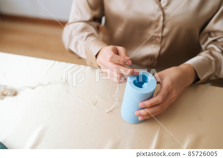 Close-up high-angle view of unrecognizable female artisan putting wick through silicone mold preparing for pouring liquid wax. 85726005